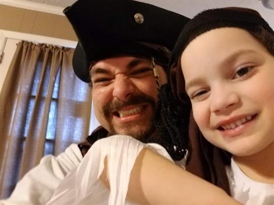 A father and daughter enjoy a playful moment while dressed as pirates in their living room.