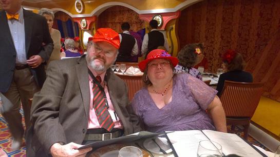 A cheerful couple shares a moment at a festive dinner, both wearing bright red hats.