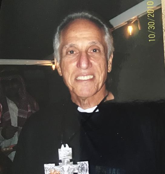 A friendly elderly man wearing casual clothing enjoys a social moment with others, smiling brightly.