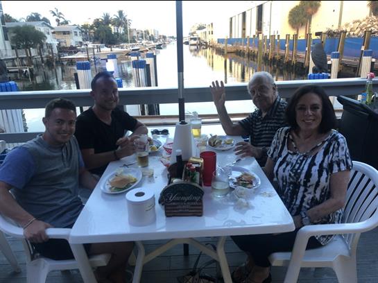 Group of four enjoying a meal together by the water, laughing and sharing stories at sunset.