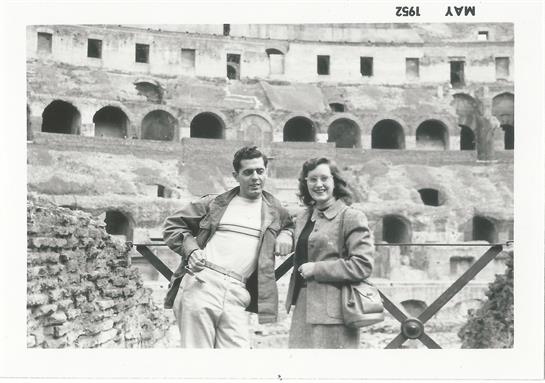 Two tourists pose together at the ancient Colosseum, showcasing its historic architecture.