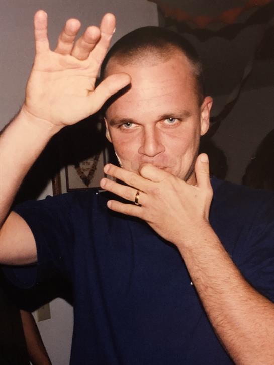 A man is playfully gesturing with his hands and smiling in a lively indoor atmosphere.