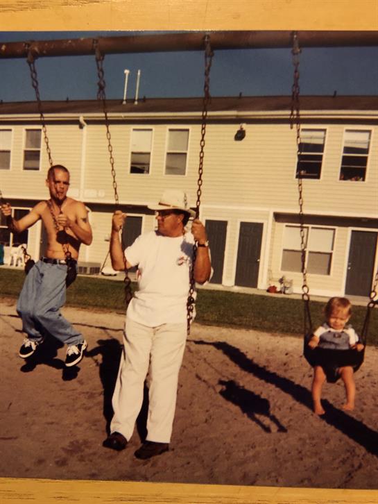 Three individuals are having fun on swings at a playground, enjoying the warm weather.
