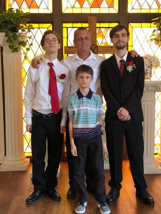 Four family members stand together in formal clothes inside a wedding venue, smiling happily.