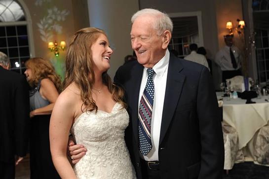 A young bride in a white dress smiles at her grandfather while they share a heartfelt moment.