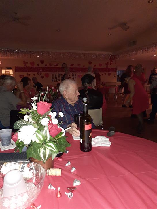 An elderly man at a red table enjoys the lively dance party with friends around him.