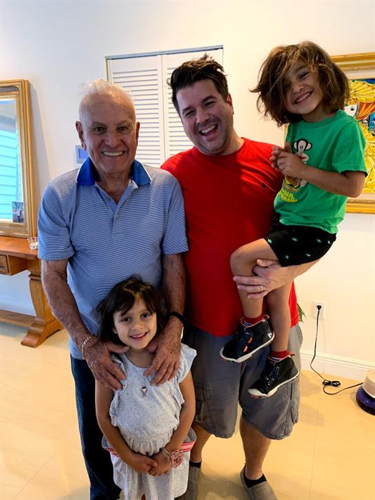 A grandfather poses with his son and two happy grandchildren in a cheerful setting.