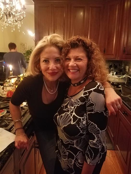 Two friends smile and embrace in a warmly lit kitchen filled with food and decorations.