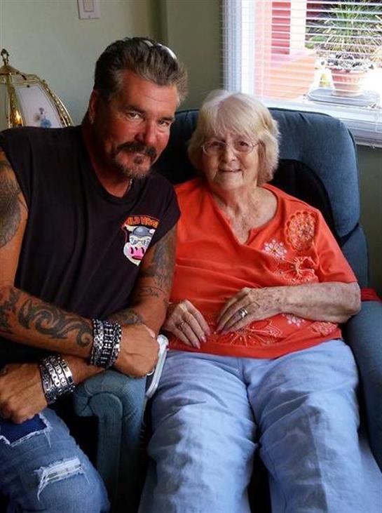 A man and an elderly woman sit together, smiling in a cozy living room.