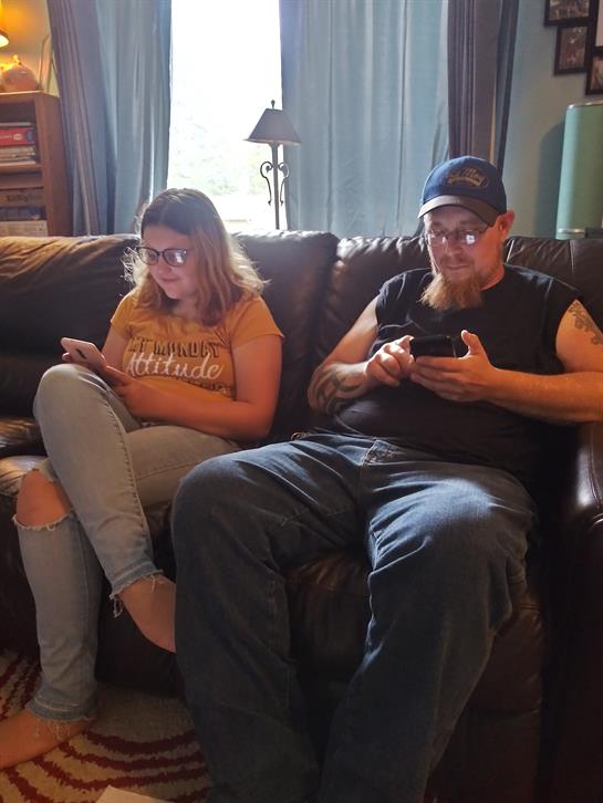 Friends relax on a couch, each absorbed in their smartphones, in a comfortable living room.