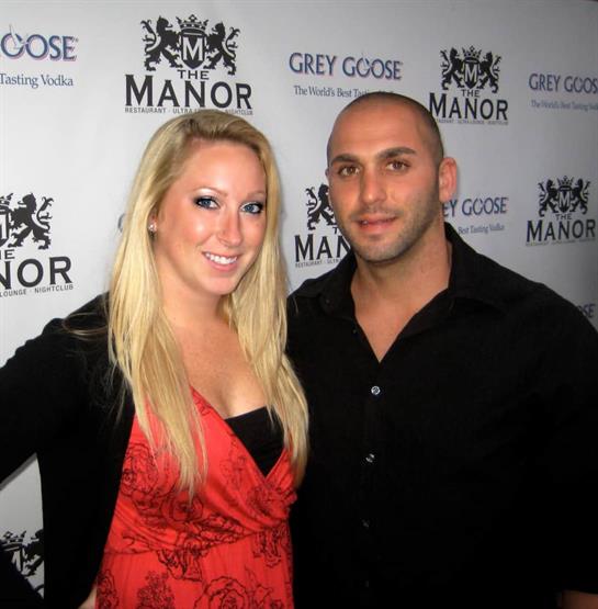 A couple smiles together at a stylish event, showing off their fashion choices.