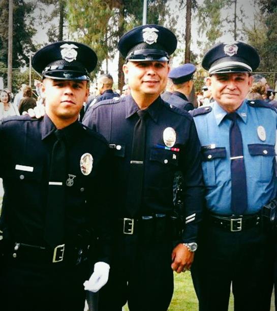 Officers stand proudly in uniforms, smiling with a backdrop of greenery and people.