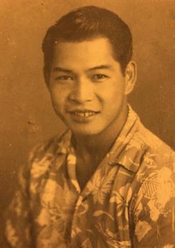 A young man stands smiling confidently in a floral shirt, captured in sepia tones.