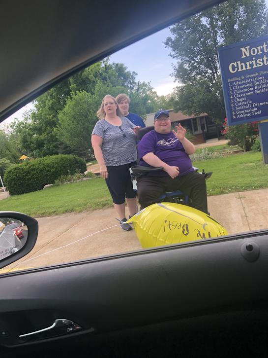 Three individuals enjoy a moment outside a local venue, smiling and waving at passersby.