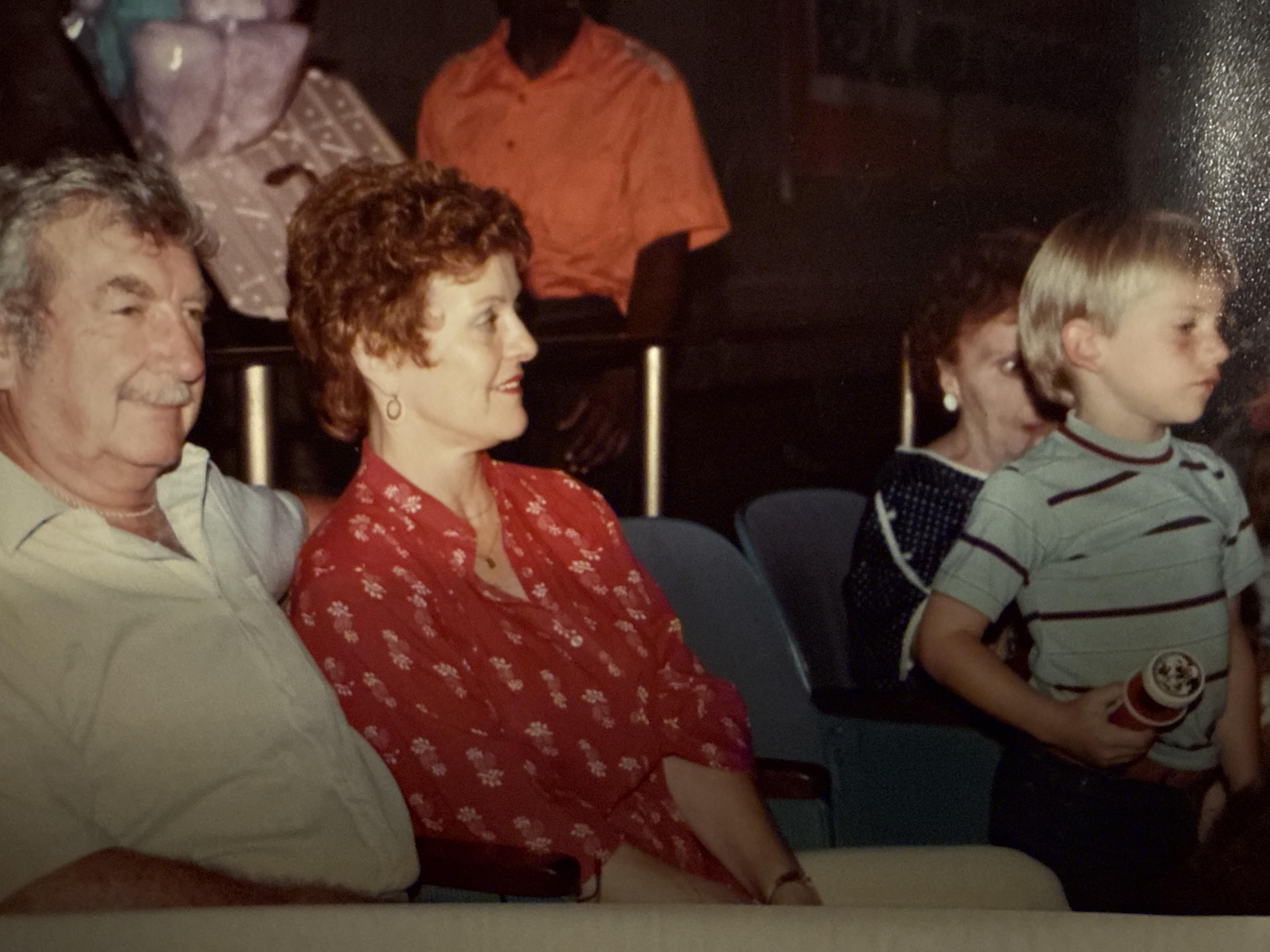 Two adults and a child are seated in a theater. They watch a performance and share smiles.