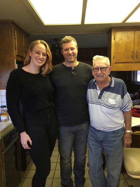 Three family members stand smiling in a warm kitchen, enjoying a special moment together.