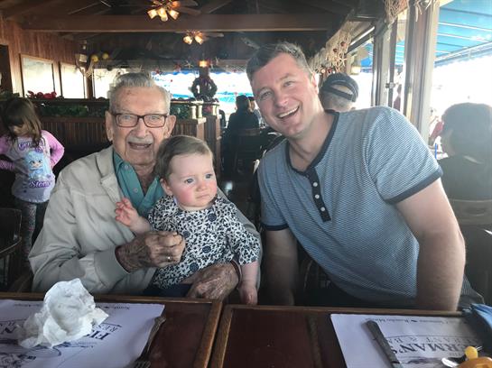A grandfather, father, and baby share a joyful meal in a cozy coastal eatery.
