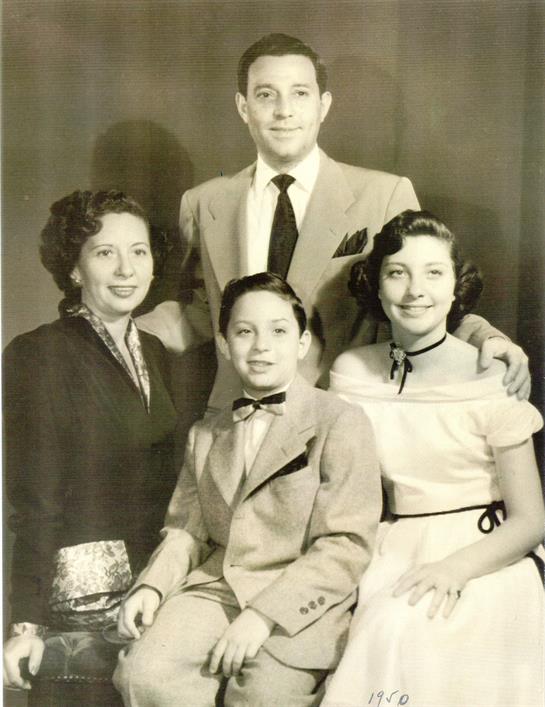 A family poses closely for a formal mid-1900s portrait in a studio, showing off their outfits.