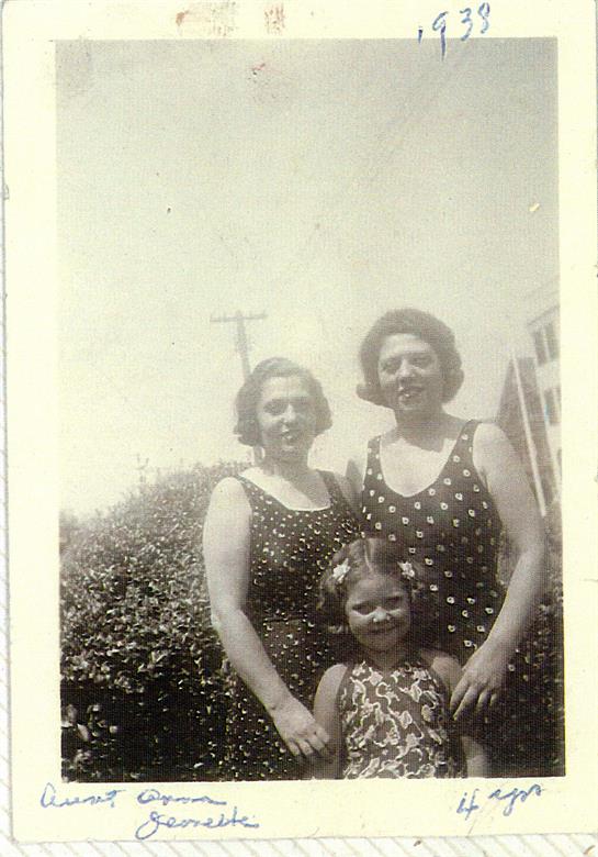 Two women stand with a girl in polka dot dresses, smiling in a sunny outdoor setting.