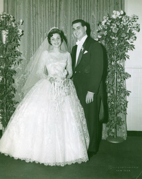 A joyful couple in wedding attire stands amidst floral decorations at their celebration.
