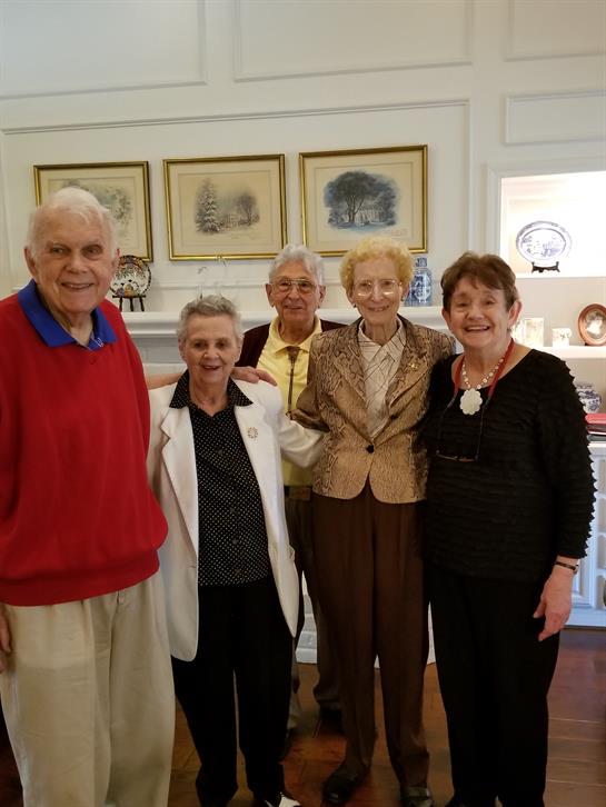 Five seniors smile together in a cozy living room, enjoying an afternoon gathering.