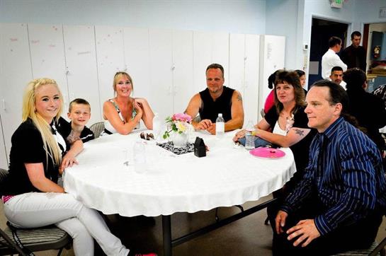 Group of six friends sharing laughter and stories around a round table with refreshments.