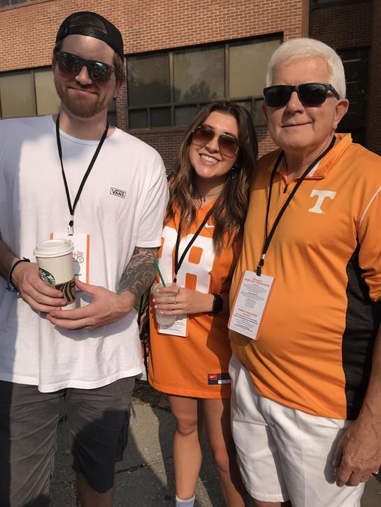 Three fans enjoy a sports event outside a stadium, wearing team colors and sharing drinks.