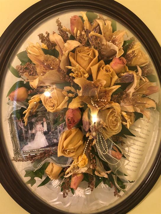 A beautiful arrangement of yellow roses and other flowers is framed and hanging on the wall.