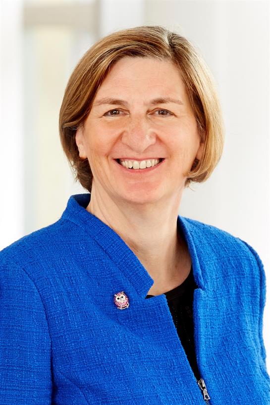 An individual in a blue blazer showcases a welcoming smile against a light office backdrop.