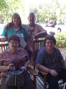 Four women enjoy a moment together on a sunny day in a warm and inviting outdoor space.