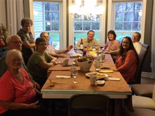 A group of family members enjoys dinner and conversation at a large table in a warm home setting.