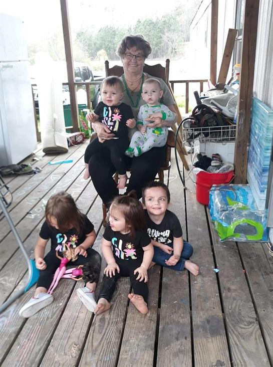 A cheerful gathering of small children and a woman takes place on a rustic porch.