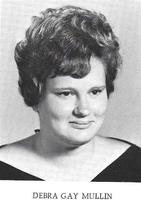A young woman with curly hair is smiling softly against a neutral background, exuding warmth.