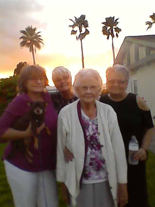 Four women stand together outside, enjoying each other's company at sunset near palm trees.