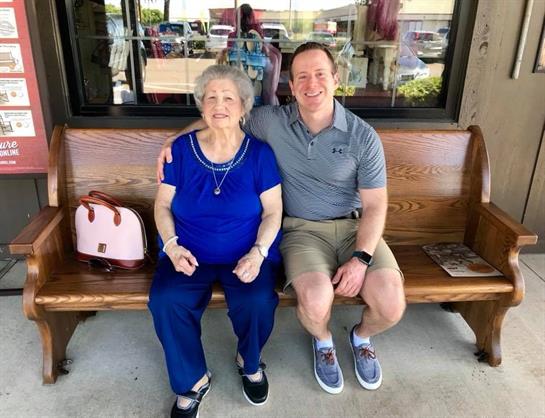 A joyful elderly woman in blue sits with a smiling man on a cafe bench, enjoying togetherness.
