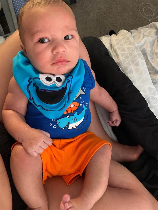 Baby appears relaxed while sitting on a parent's lap, wearing a fun outfit and shorts.