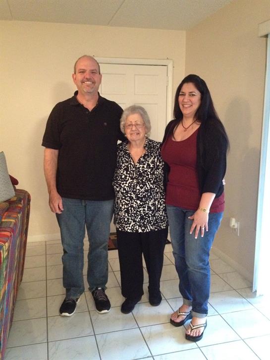 Three family members stand together, smiling in a comfortable living room filled with warmth.