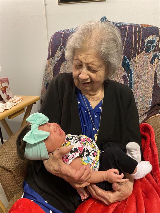 Grandmother smiles as she cradles her newborn granddaughter in her arms, sharing a tender moment.