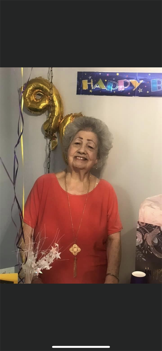 A woman dressed in red smiles brightly during a birthday celebration surrounded by balloons.