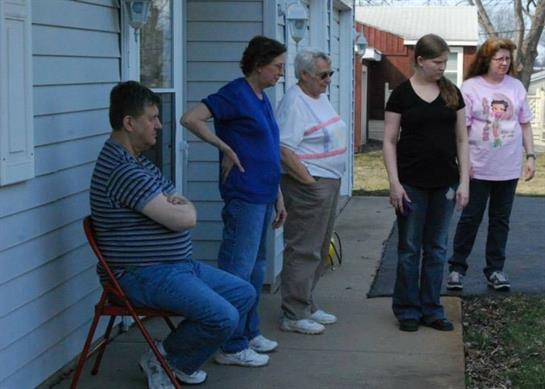Four individuals share a moment outside a house, engaged in discussion and enjoying the day.