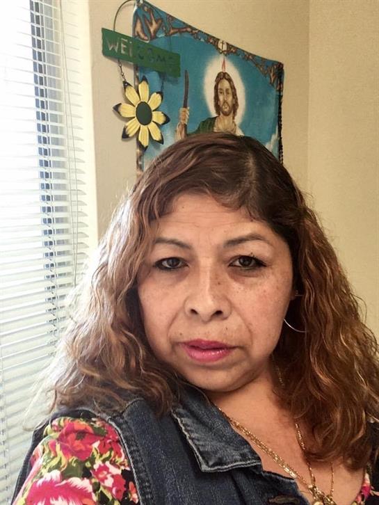 A woman with curly hair in a floral blouse smiles in a bright room with religious art.