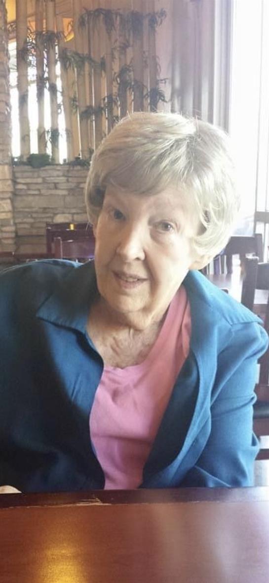 A happy elderly woman in a blue jacket enjoys a cozy restaurant atmosphere.