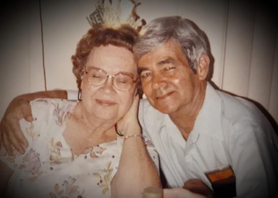 Elderly couple shares a loving moment while celebrating with friends and family at home.