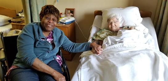 A caregiver smiles, holding hands with an elderly patient in a moment of comfort.