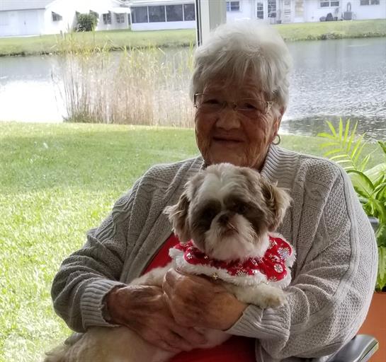 An elderly woman relaxes outdoors with her small dog in a peaceful garden.