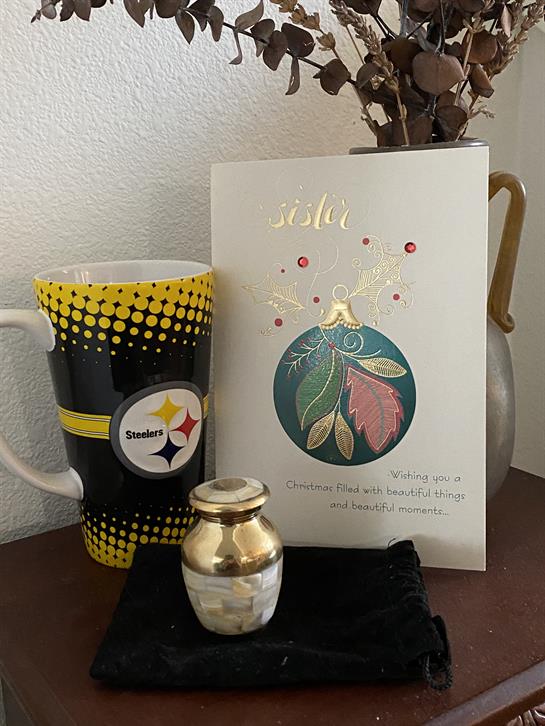 A decorative table showcases a coffee mug, an urn, and a heartfelt card celebrating sisterhood.