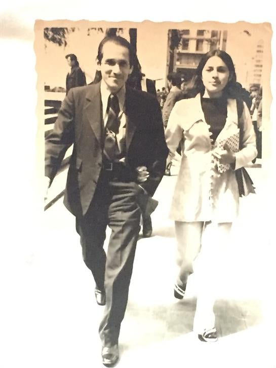A couple strolls down a busy sidewalk, enjoying the vibrant city atmosphere on a warm day.