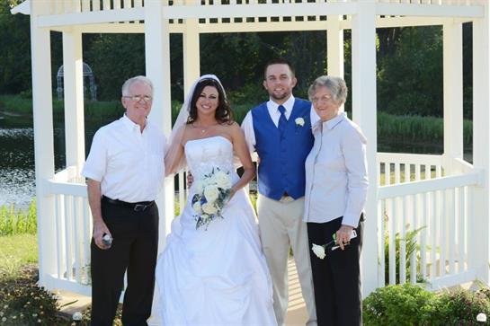 A joyful bride and groom pose with their grandparents at a garden wedding during daylight.