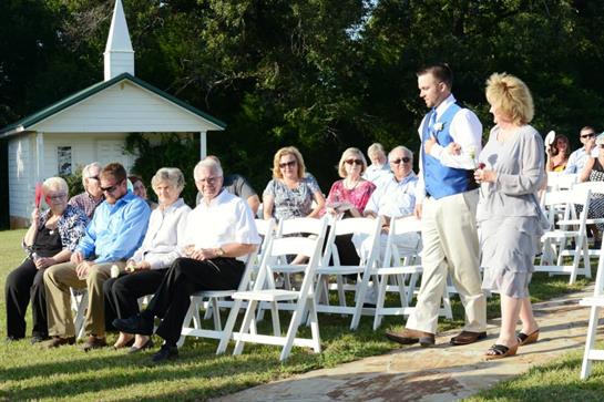 Guests sit in white chairs watching the wedding ceremony at a beautiful outdoor venue.