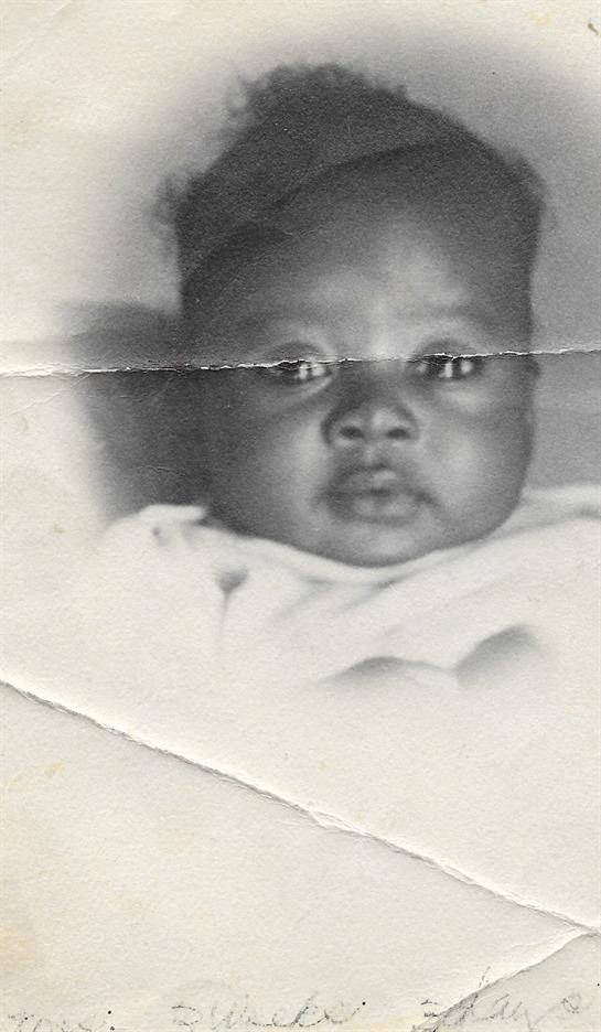 A baby gazes intently at the camera in a vintage black and white portrait, showing innocence.